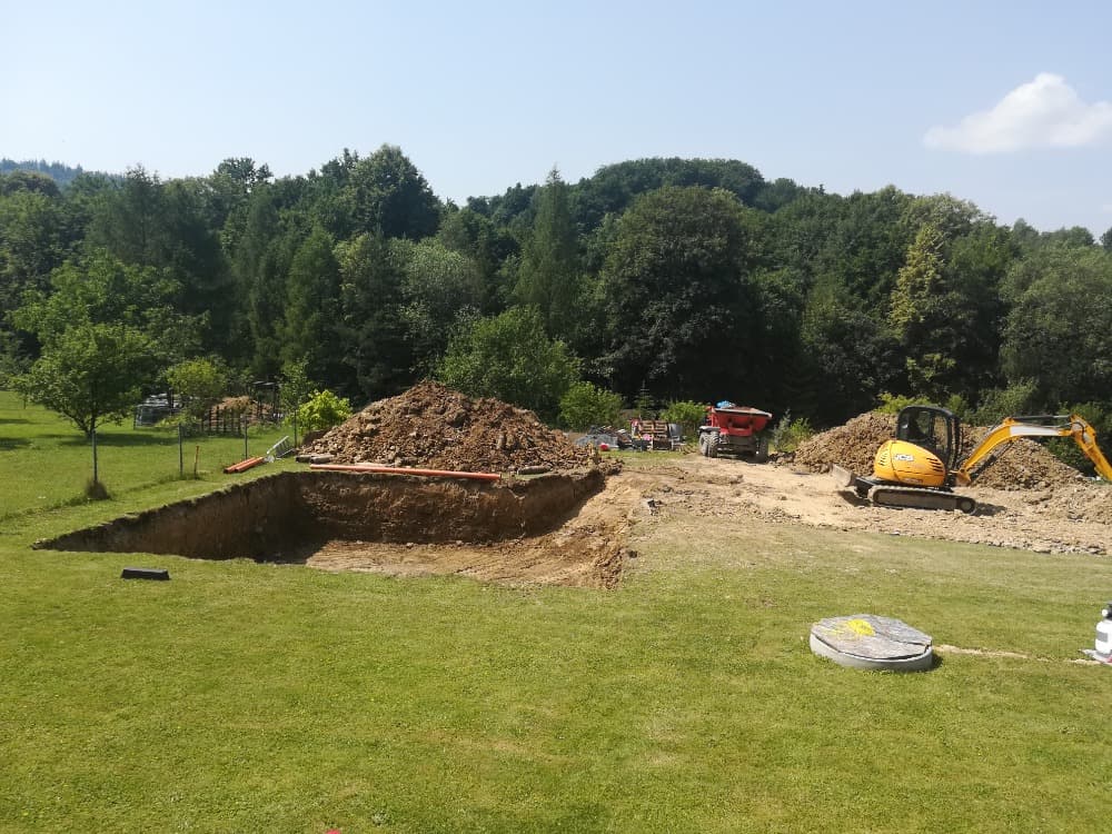 Výkop jámy na travnaté zahradě s panoramatem beskydských kopců v pozadí