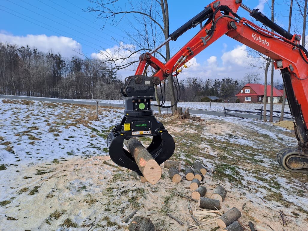 Pásový bagr Kubota s hydraulickým drapákem manipuluje s kmeny stromů v zimním terénu