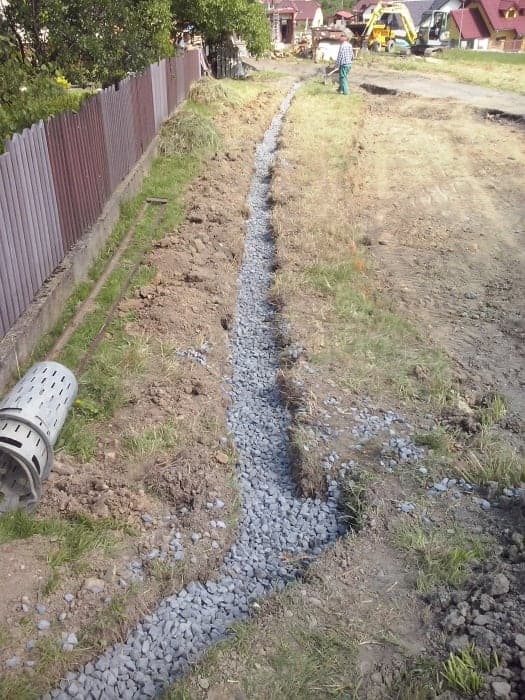 Vykopaná drenážní rýha vysypaná drceným kamenivem podél plotu
